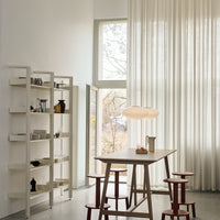 Modern dining space featuring soft beige tones, sheer white curtains, and warm red accents on stools.