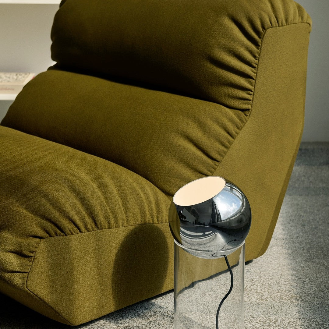 Olive green sofa with plush fabric and a sleek, modern chrome lamp on a transparent base. Elegant and contemporary design.