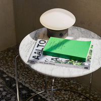 White marble table topped with a green book and magazines, featuring a soft-glow round lamp. Modern and stylish design.