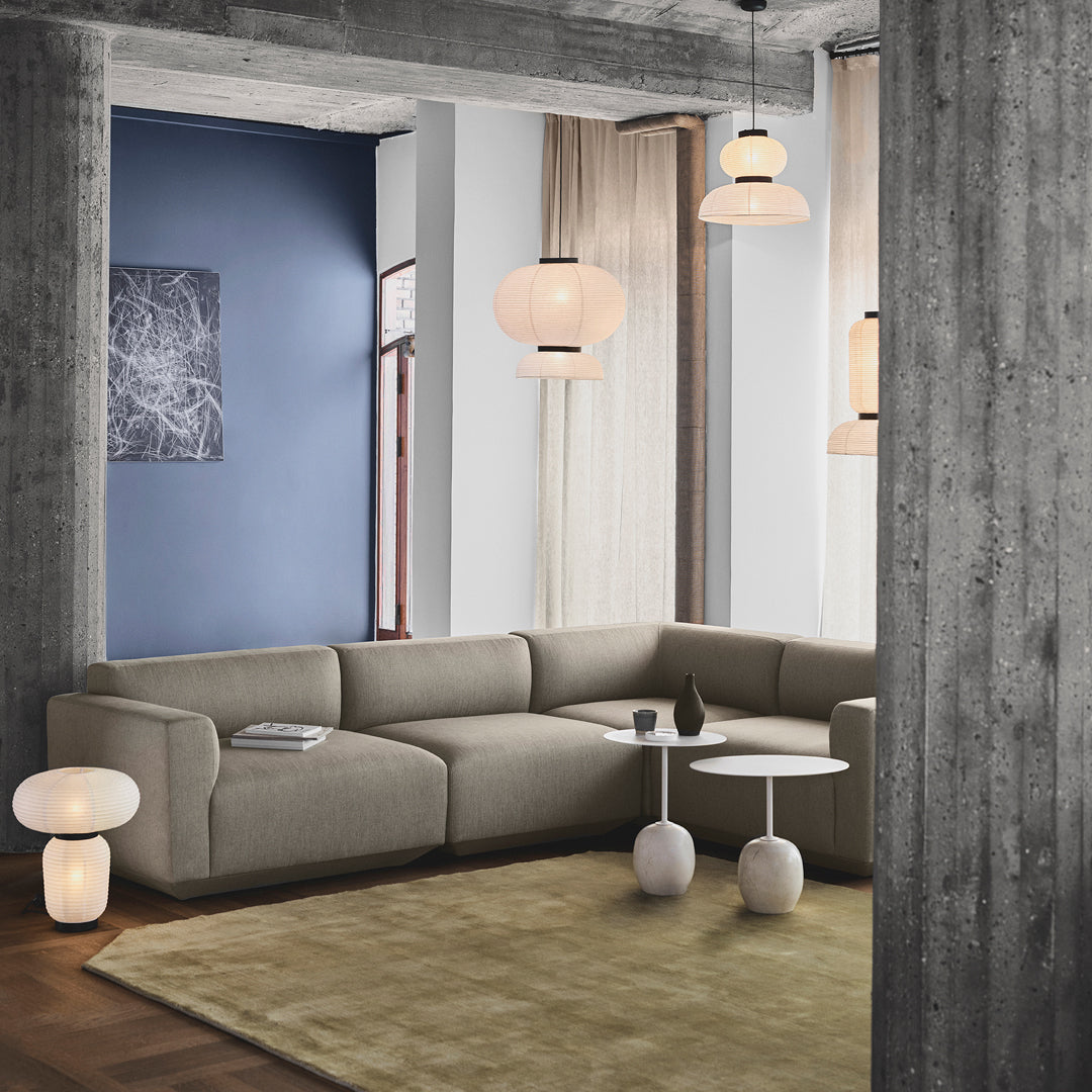 Modern living room with a beige sectional sofa, soft green rug, blue accent wall, and warm-toned lighting.
