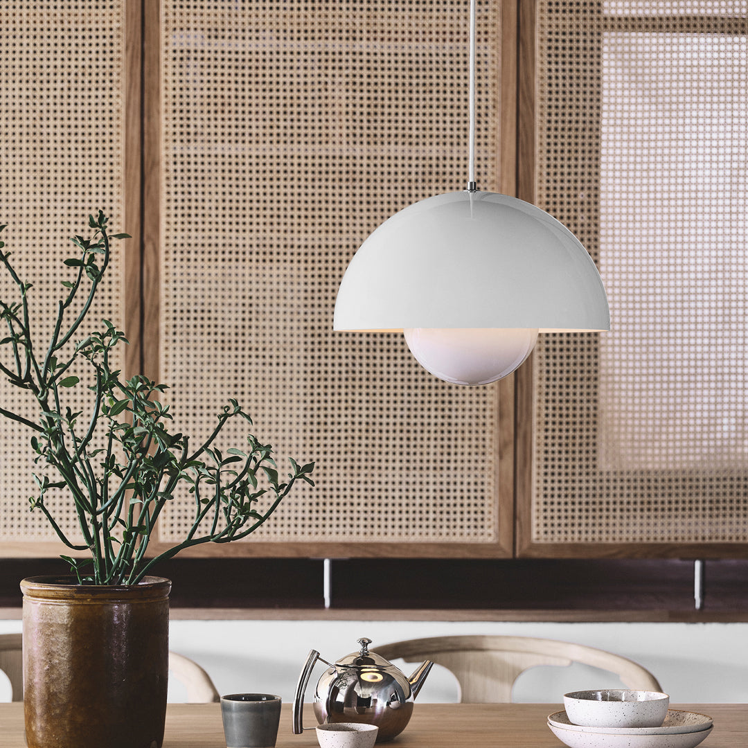 Sleek white pendant lamp with a domed shade, complemented by a warm, soft glow, against a textured natural backdrop.