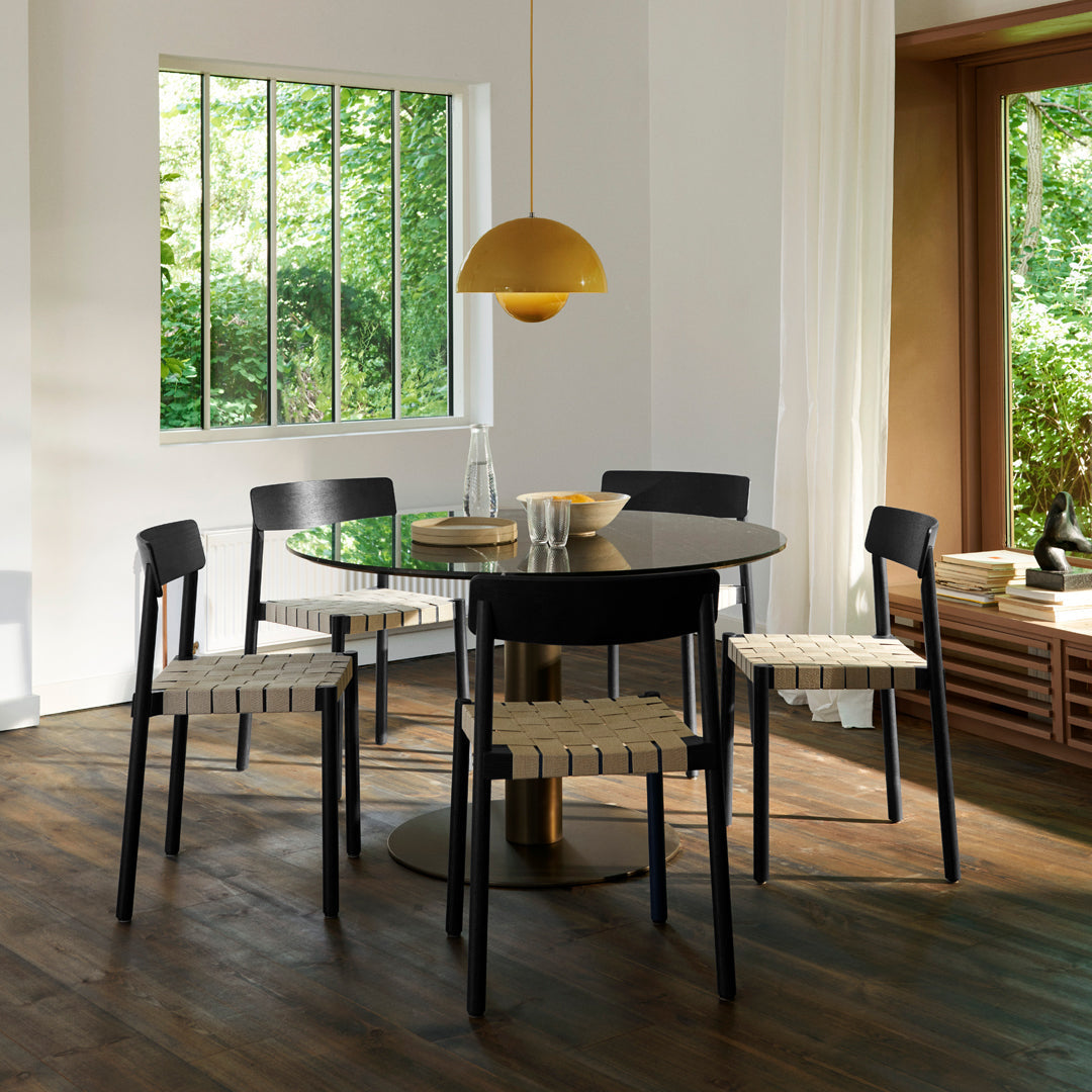 Modern black dining set with woven beige chairs, featuring a sleek round table and warm golden pendant light.
