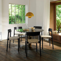 Modern black dining set with woven beige chairs, featuring a sleek round table and warm golden pendant light.