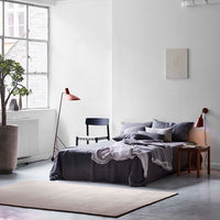 Modern bedroom featuring gray bedding, white walls, and soft pastel accents with a neutral area rug.