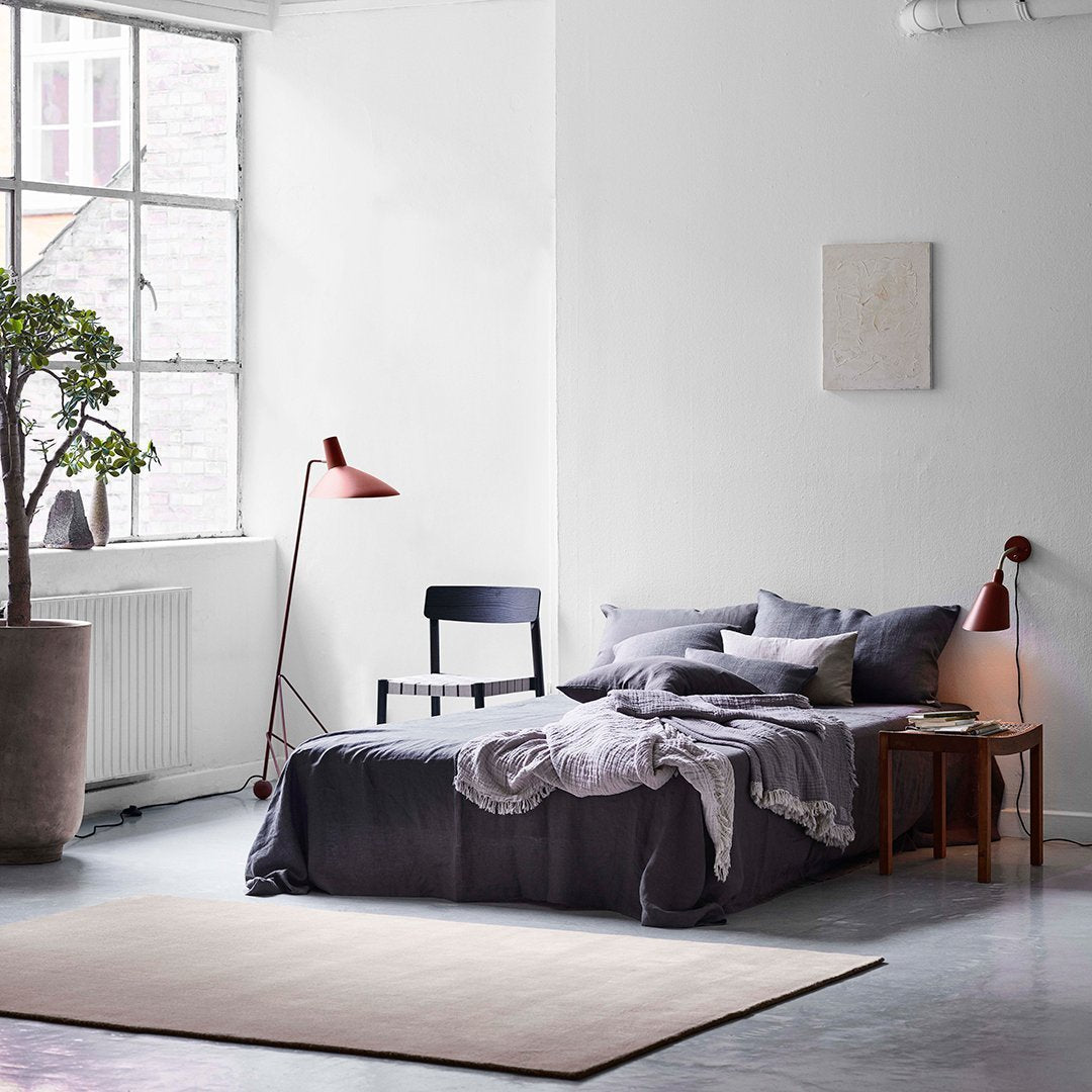 "Neutral-toned bedroom featuring gray bedding, a muted rug, and earthy green plant accents."