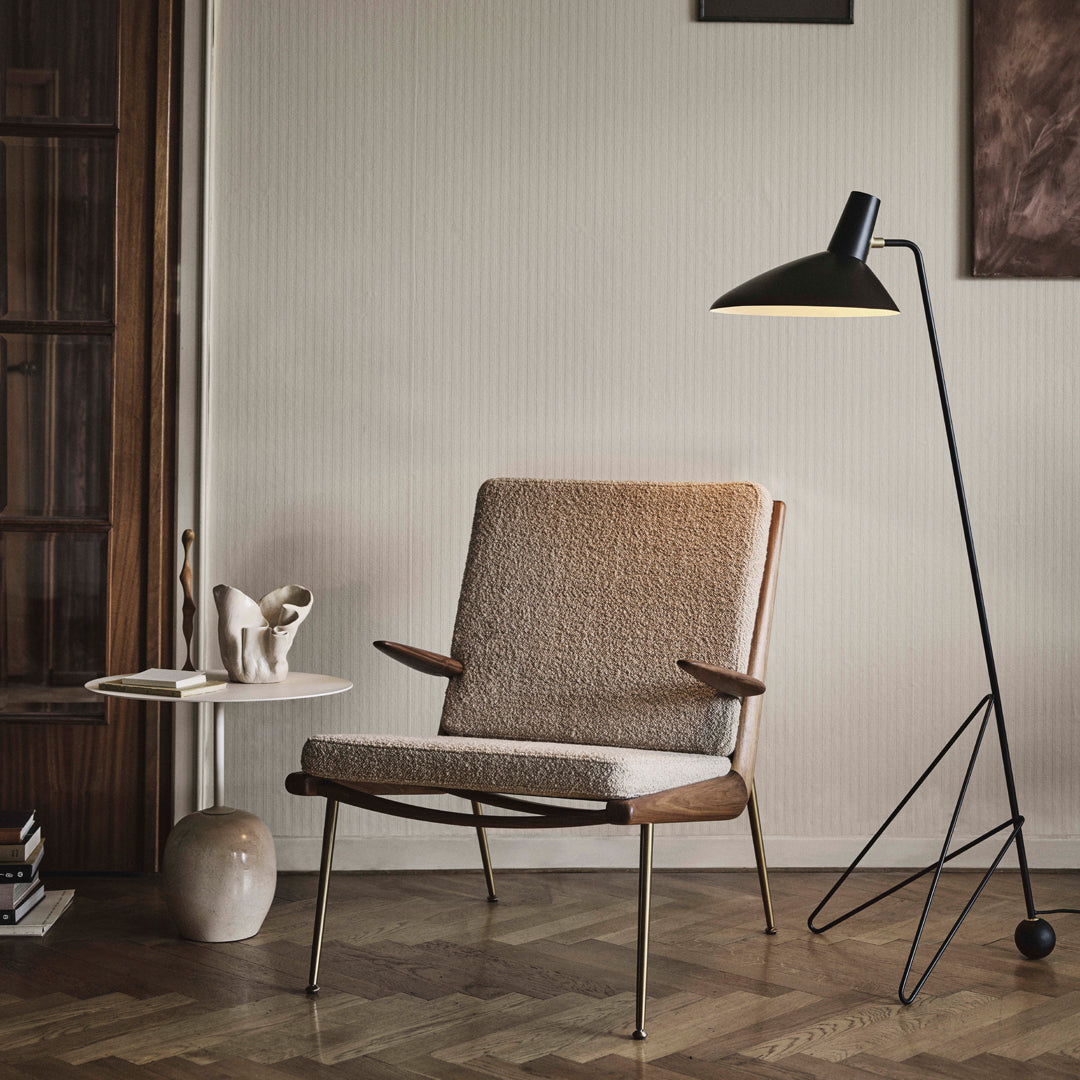 Mid-century modern chair with a warm beige fabric and natural wood finish, complemented by a black and gold floor lamp.