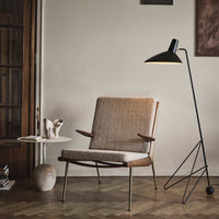 Mid-century modern chair with a warm beige fabric and natural wood finish, complemented by a black and gold floor lamp.