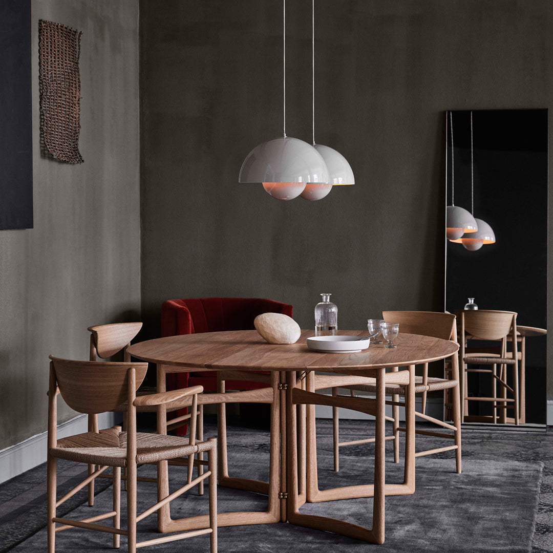 Modern dining room featuring a round wooden table, beige curtains, red velvet chair, and minimalist light fixtures.