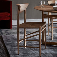 Natural wood chair with a woven seat, featuring light oak tones and geometric patterns, set against a textured gray rug.