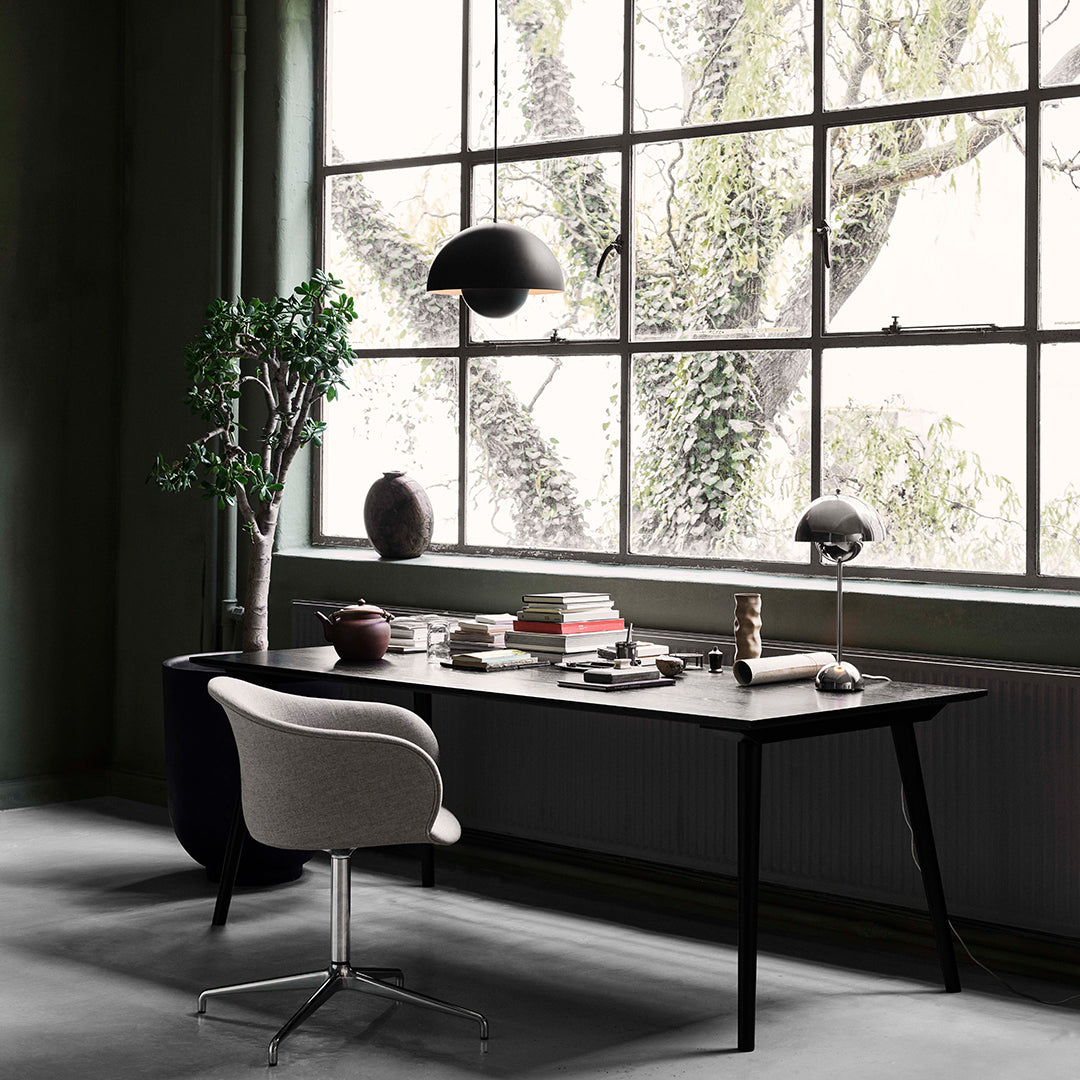 Modern black office desk with a neutral chair, surrounded by green walls and natural light filtering through large windows.