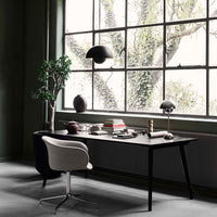 Modern black office desk with a neutral chair, surrounded by green walls and natural light filtering through large windows.