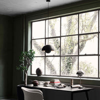 Stylish office scene featuring deep green walls, a minimalist black lamp, and soft beige accents. Nature-inspired patterns outside.