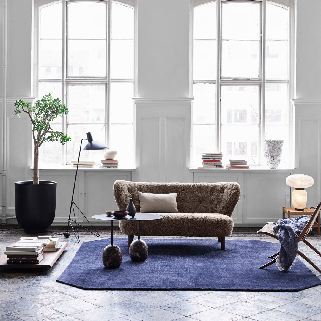Beige sofa on a navy rug, with natural wood accents and greenery in a bright, airy room. Modern, minimalist design.