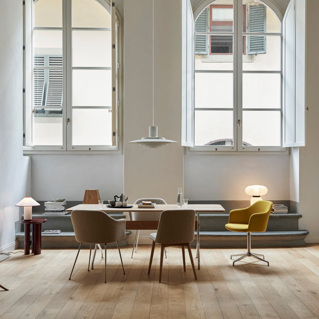 Modern workspace featuring light wood flooring, neutral chairs, and a pop of yellow from an accent chair. Natural light streams in.