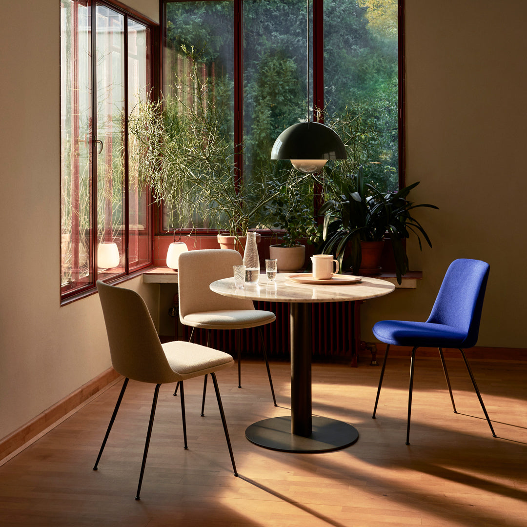 Modern dining set featuring beige, blue, and cream chairs around a round marble table in a sunlit room.