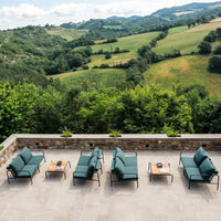 "Outdoor seating set in deep teal with stylish wood accents, against a lush green hillside backdrop."