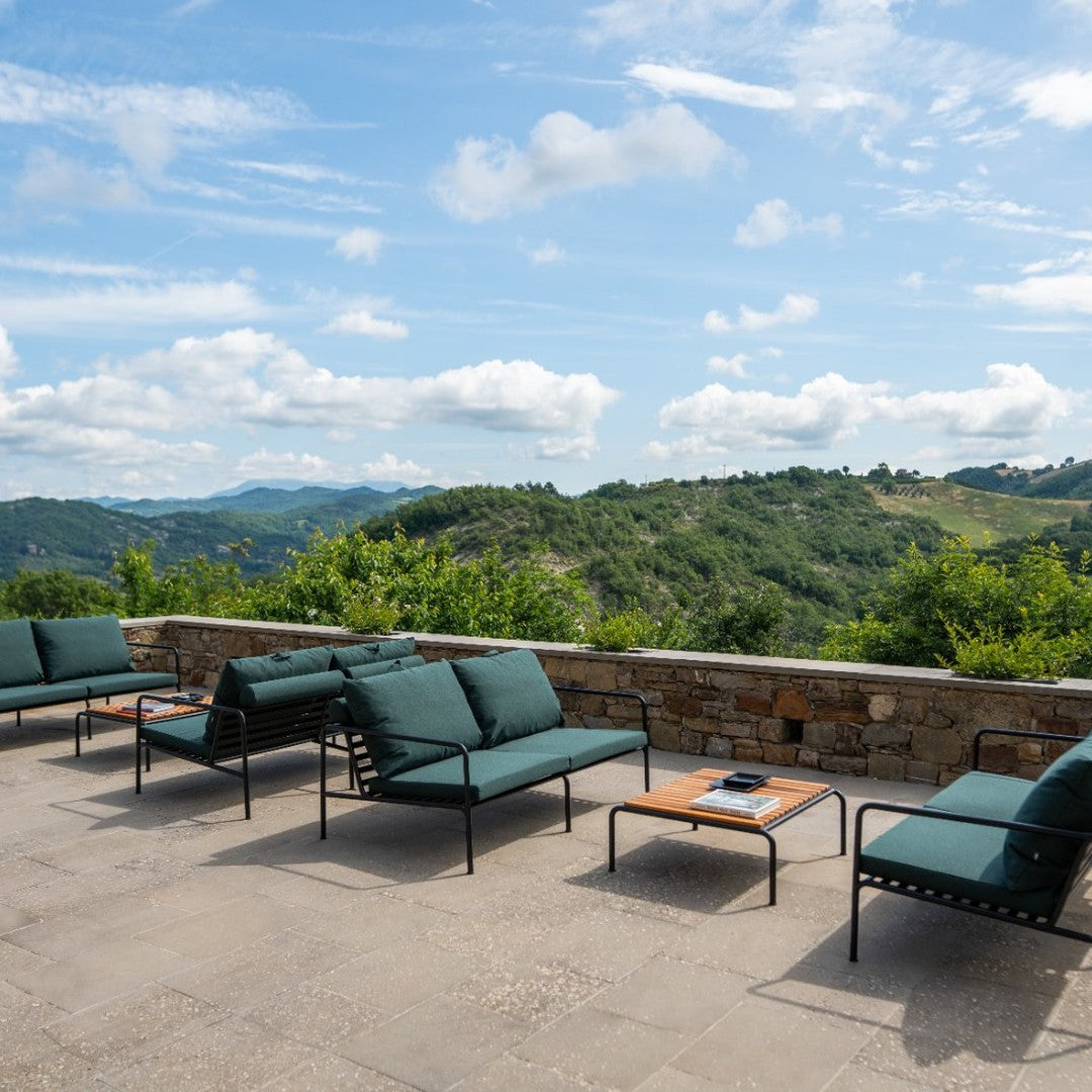 Teal outdoor cushions on black metal frames, paired with a wood coffee table against a scenic green landscape.