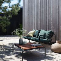 Stylish green cushions on a modern black frame sofa with a wooden coffee table in a natural outdoor setting.