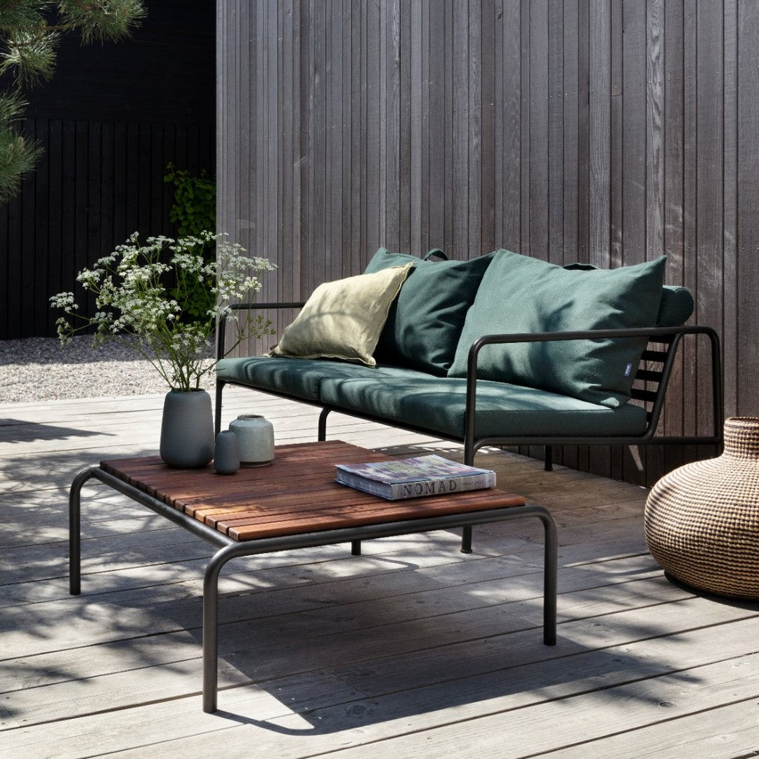 Green and blue cushions on a black metal sofa, paired with a wooden coffee table and neutral decorative items.