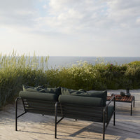 Black metal frame sofa with green cushions, set against a natural landscape and ocean backdrop. Ideal for outdoor spaces.