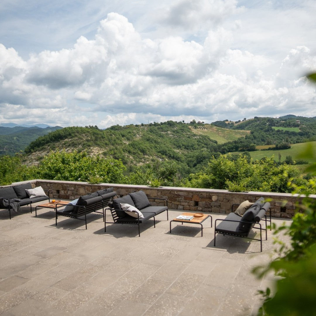 "Dark gray outdoor lounge chairs with natural wood accents against a lush green landscape and cloudy sky."