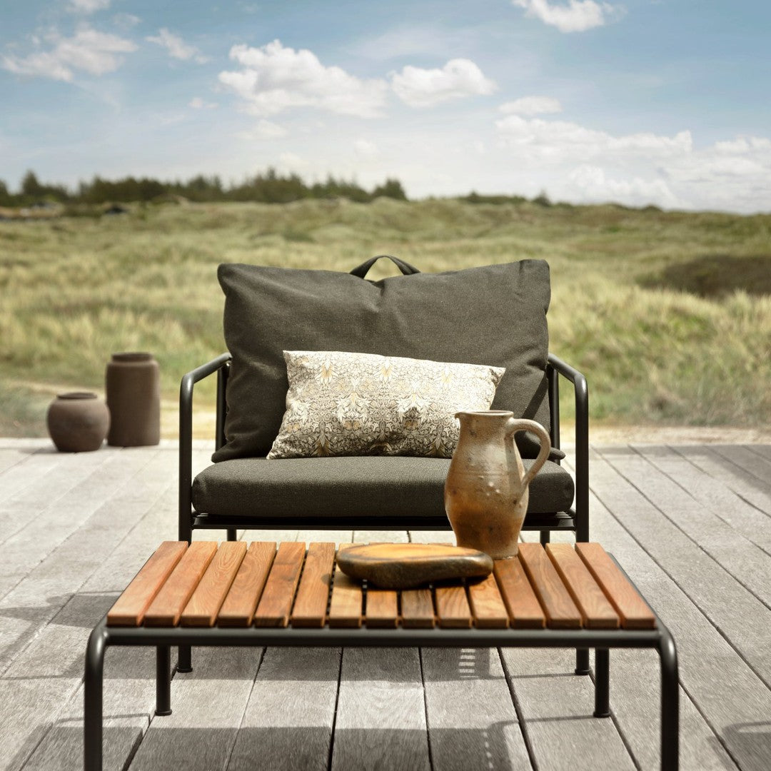 "Cozy outdoor chair in charcoal gray with a patterned pillow on a wooden slatted table against a natural landscape."