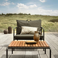 "Cozy outdoor chair in charcoal gray with a patterned pillow on a wooden slatted table against a natural landscape."