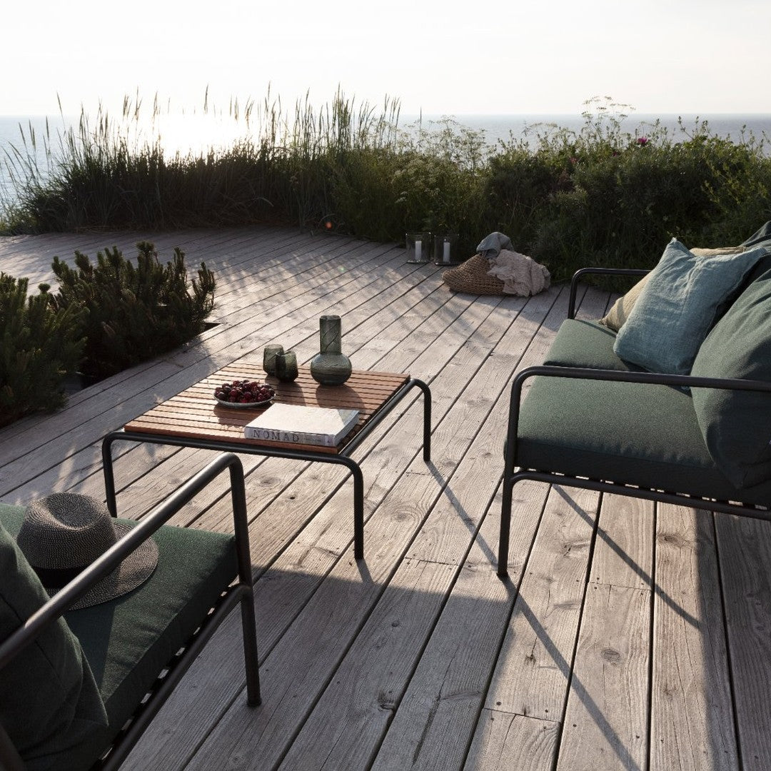 "Cozy outdoor seating with deep green cushions, black metal frame, and natural wood table on a sunlit deck."