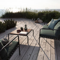 "Cozy outdoor seating with deep green cushions, black metal frame, and natural wood table on a sunlit deck."