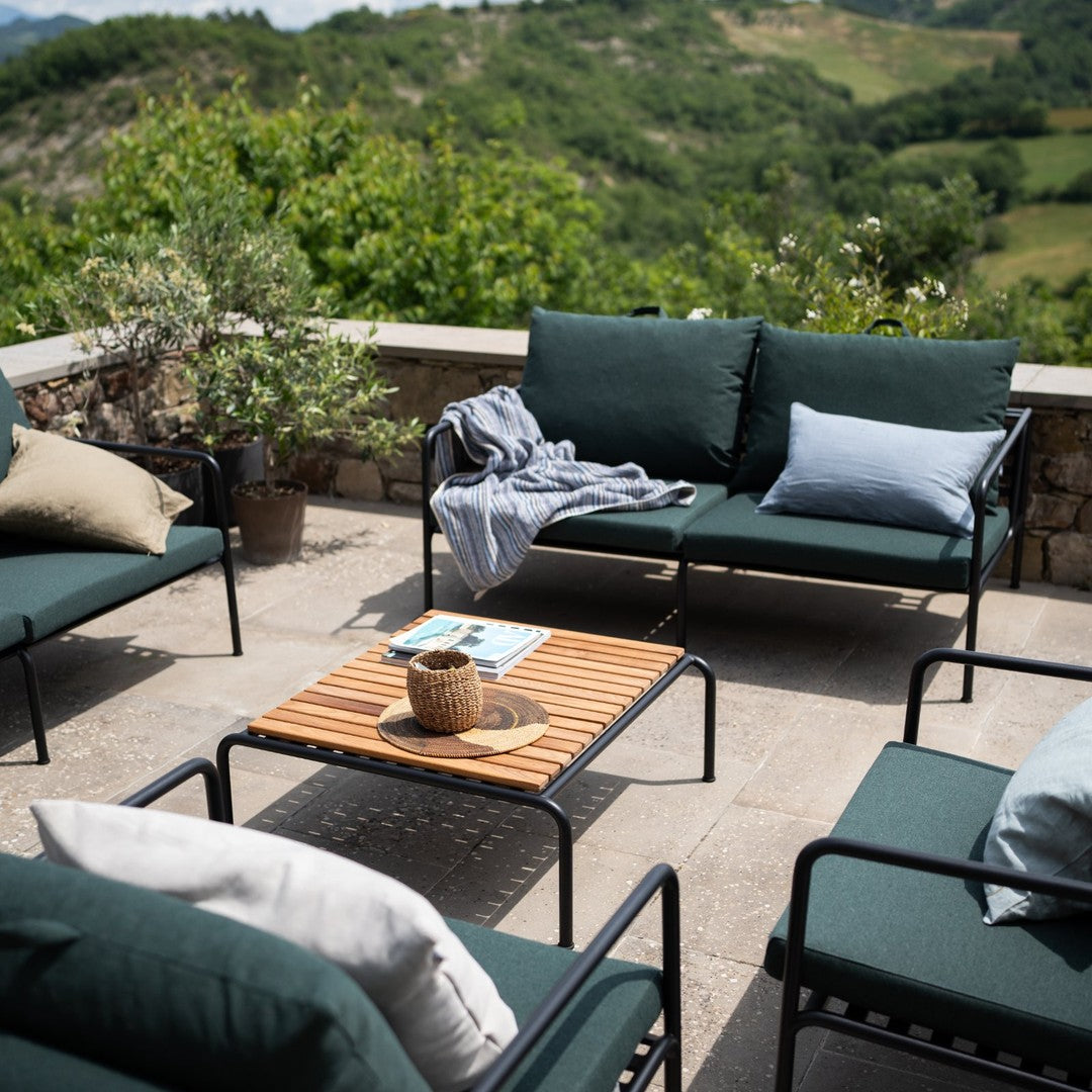 Modern outdoor furniture in dark green and light blue fabrics, featuring a natural wood table and neutral throw pillows.