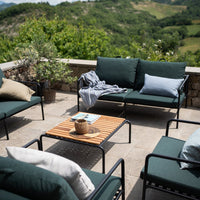 Modern outdoor furniture in dark green and light blue fabrics, featuring a natural wood table and neutral throw pillows.