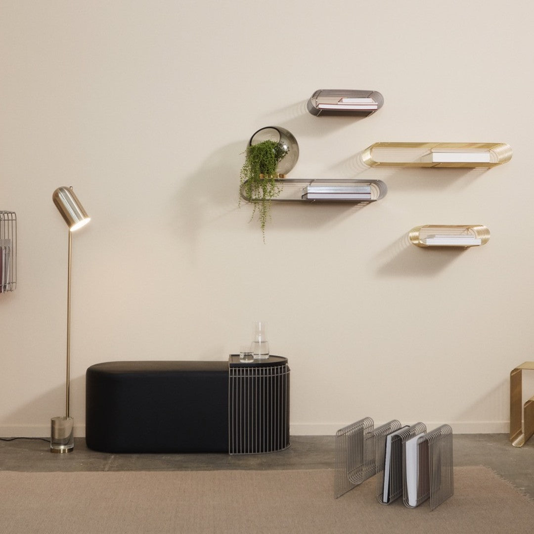 Modern shelving in gold and silver tones on a neutral wall, with a sleek black table and subtle greenery.