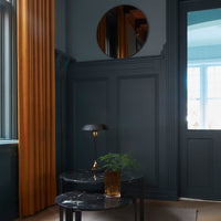 Elegant dark blue walls with golden-yellow curtains, a marble-patterned table, and a round mirror accenting the decor.