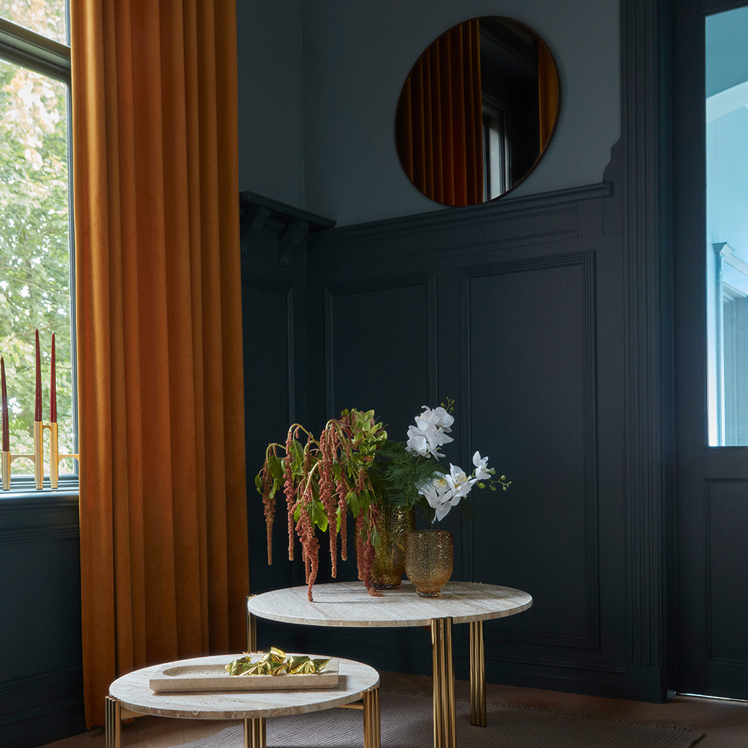 Elegant gold-accented coffee table with white floral arrangement, against rich blue walls and warm amber curtains.
