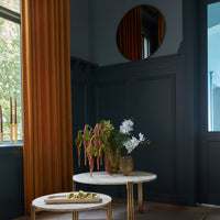 Elegant gold-accented coffee table with white floral arrangement, against rich blue walls and warm amber curtains.