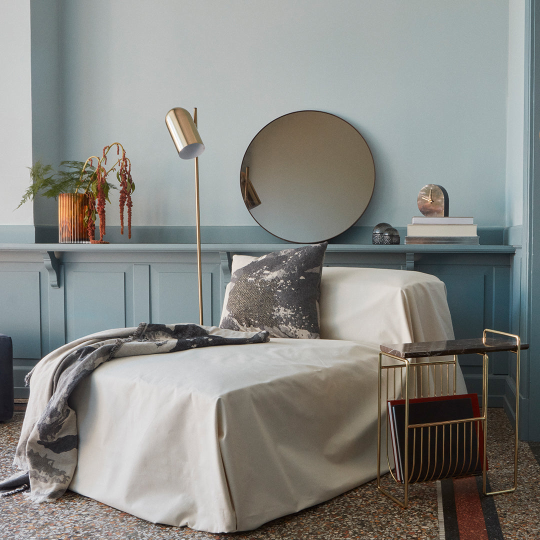 "Elegant beige and grey lounge chair with textured throw and decorative pillow against a soft blue wall."