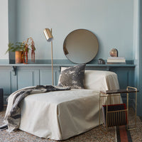 "Elegant beige and grey lounge chair with textured throw and decorative pillow against a soft blue wall."