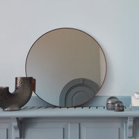 Round mirror with a sleek brown frame, reflecting soft beige and gray tones, against a light blue wall.