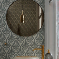 Round mirror with a gold frame against a teal wallpaper featuring a stylish art deco pattern in muted tones.