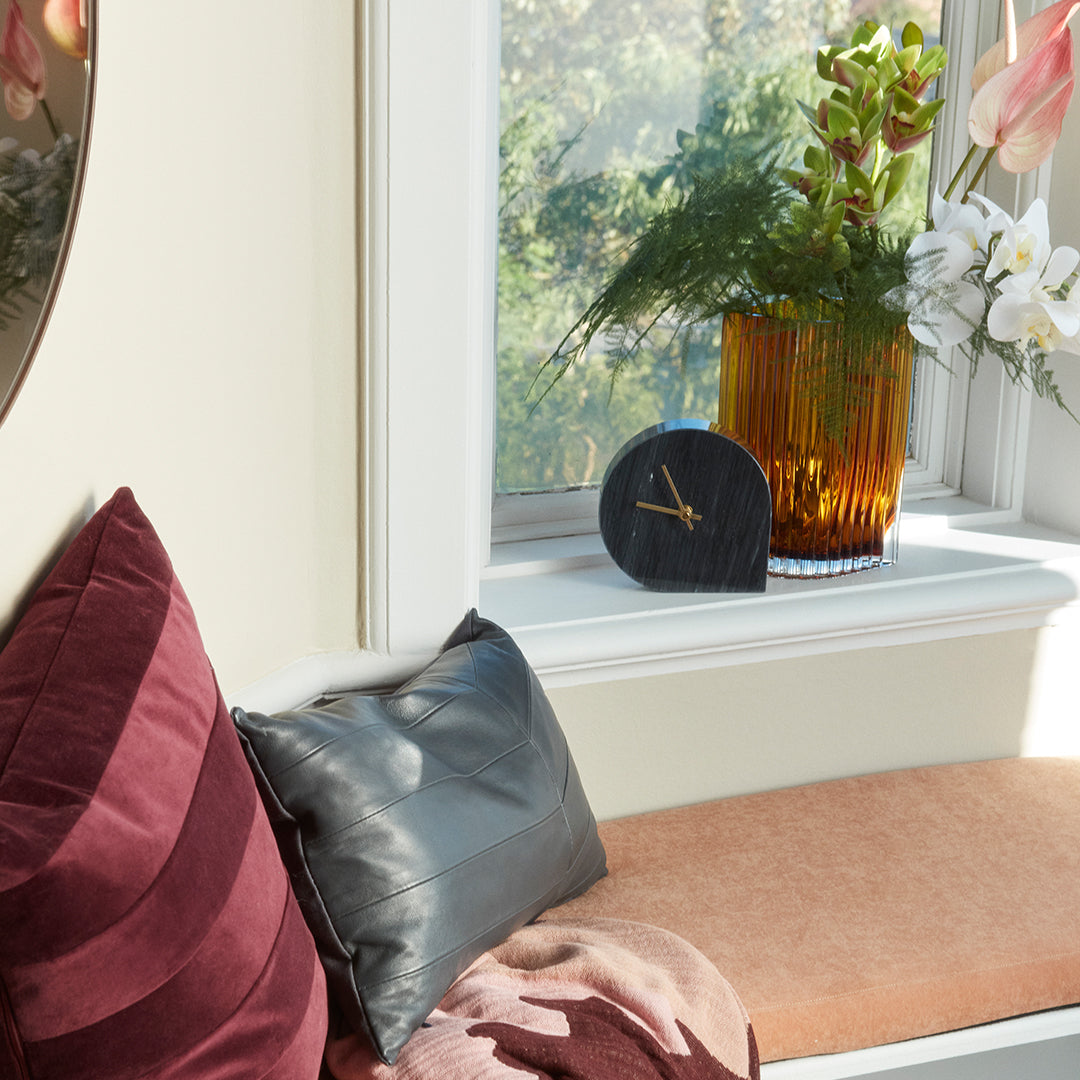 Multicolored pillows in burgundy, gray, and peach, with a striped velvet texture beside a sleek black clock.