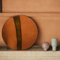 Terracotta round mirror with green stripe; two striped vases in pink and white, and striped green and white.