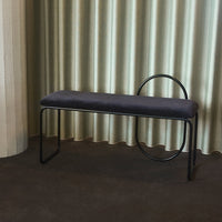 Gray upholstered bench with black metal legs and unique circular accent against soft beige curtains.