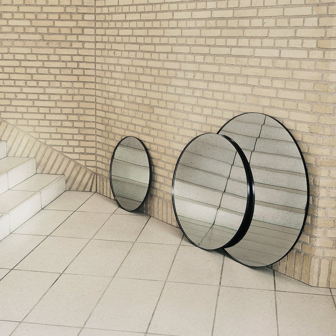 Three circular mirrors with black frames against a light brick wall, featuring a sleek, modern design.