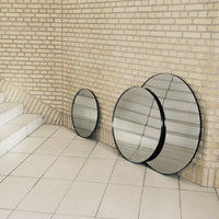 Three circular mirrors with black frames against a light brick wall, featuring a sleek, modern design.