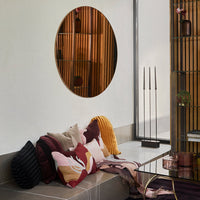 Round mirror in warm bronze, featuring patterned cushions in rich burgundy, soft pink, cream, and dark charcoal.