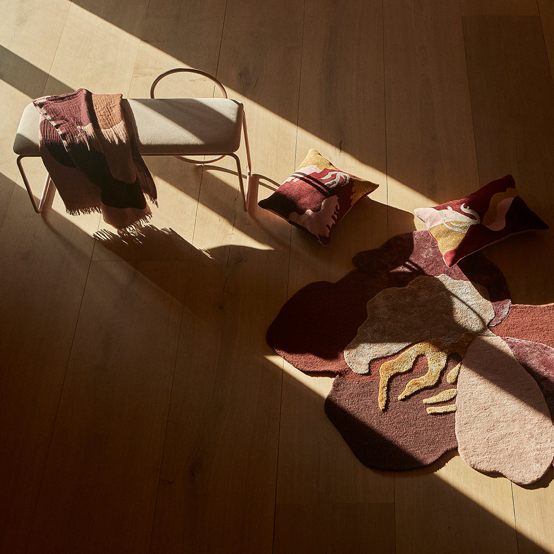 "Cozy home décor featuring earthy reds, soft pinks, and abstract floral patterns on a rug and cushions."