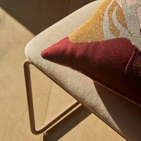 Decorative pillow with abstract patterns in burgundy, gold, and cream on a soft beige cushion. Perfect for modern décor.