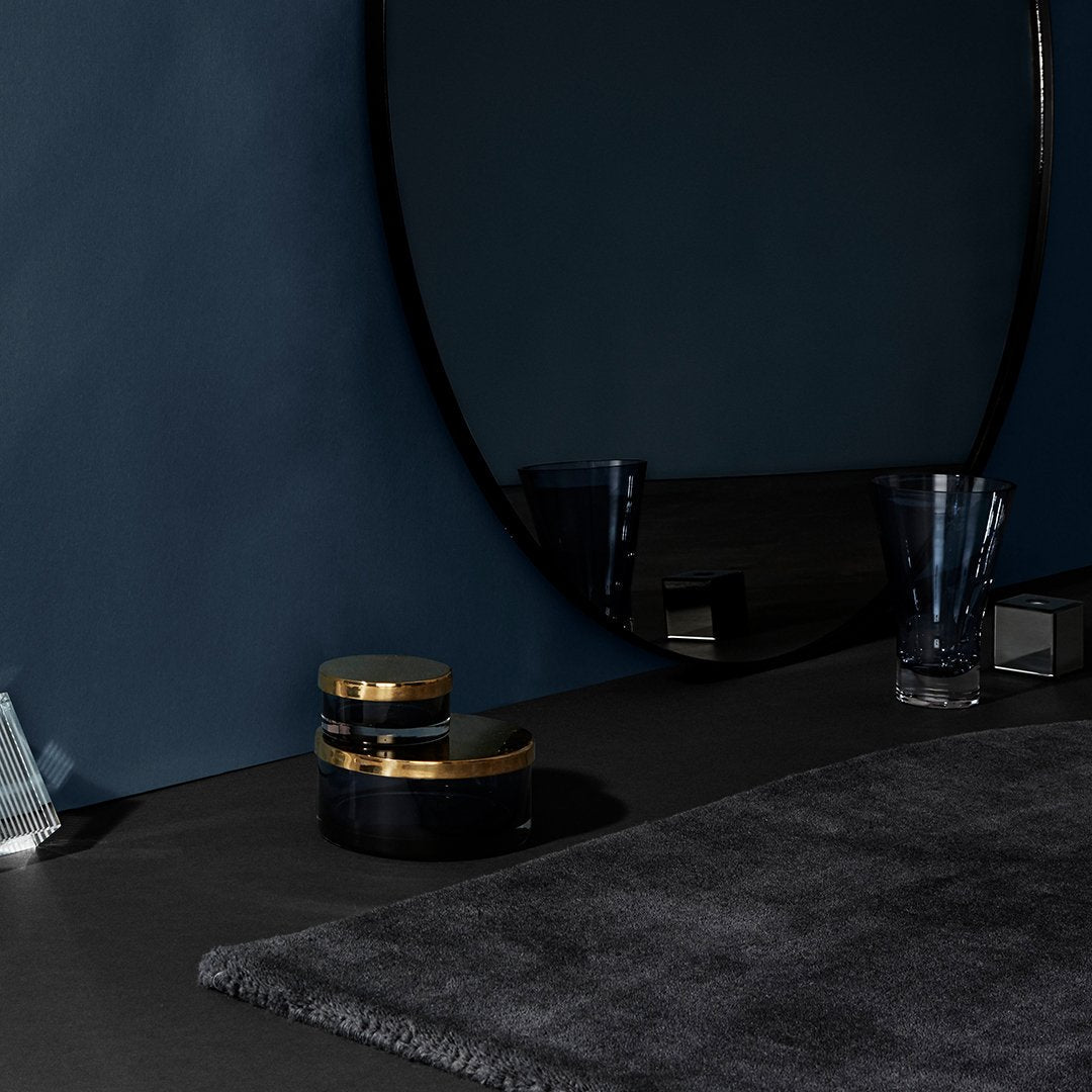 Elegant dark gray rug on a black surface with gold-accented decor against a deep blue wall.