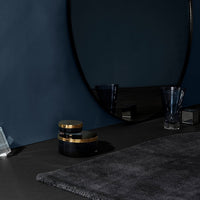 Elegant dark gray rug on a black surface with gold-accented decor against a deep blue wall.