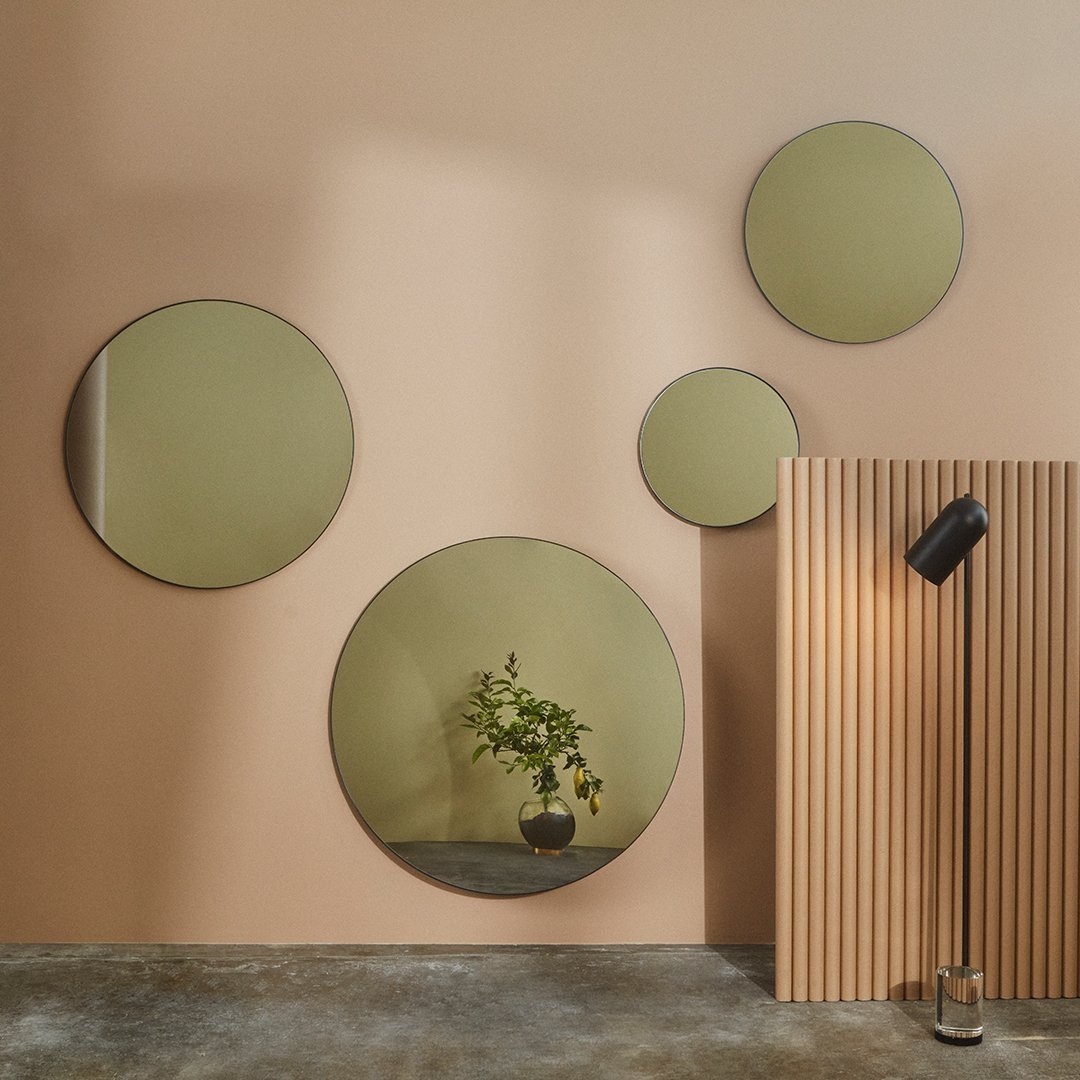 "Set of round mirrors with green-tinted reflections on a soft peach background and vertical wooden panel texture."